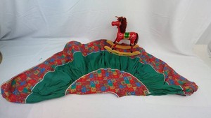 Christmas decor grouping with a colorful fabric tree skirt and a painted wooden rocking horse.  -