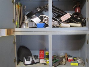 Content of shop cupboard to include magnifying lamp, sand paper, power strips, knife sharpener and other supplies shown