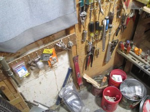 Screwdrivers, pliers, wrenches and more hanging on shop wall and workbench plus misc in containers on floor