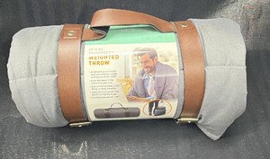 Brand New - This is a 40 x 50 therapeutic weighted throw blanket, still in its retail packaging, rolled up in a gray cover and held by removable brown faux leather straps.