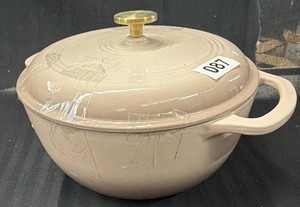 Brand New  Enameled Cast Iron Dutch oven in a blushpale pink color, with a lid topped by a brass-toned knob and two loop handles. The ringed pattern on the lid is a common design on this style of cookware.