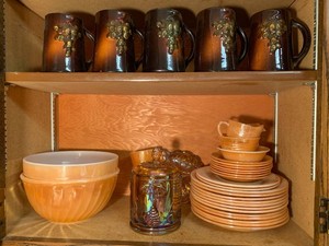 Peach luster glass, carnival glassware, Weller pottery mugs all in cupboard