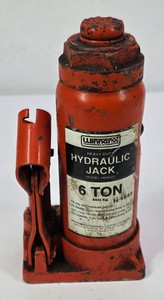 Vintage red hydraulic bottle jack marked 8 Ton, with metal base and side handle mechanism.