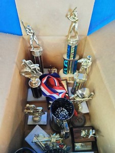 Vintage sports trophies, medallions, and a cup award featuring baseball and softball figures,