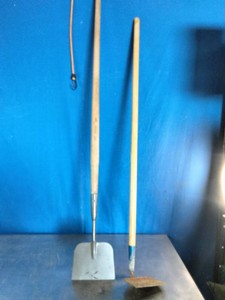 A long-handled onion hoe and  a flat metal blade and a wooden shaft,