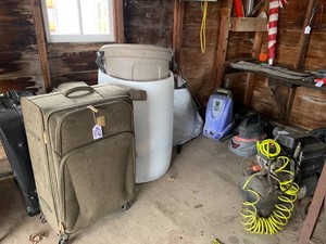 Husky vac, air compressor, car sun shield, water pump, license plates, suitcases, plastic containers, metal eagle, bags all on floor, in wall cabinet and on multiple walls of shed